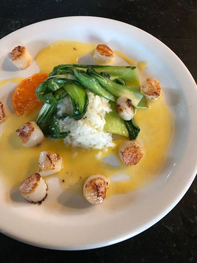 Plate of sea scallops, jasmine rice, asian greens, orange slices, and orange sauce