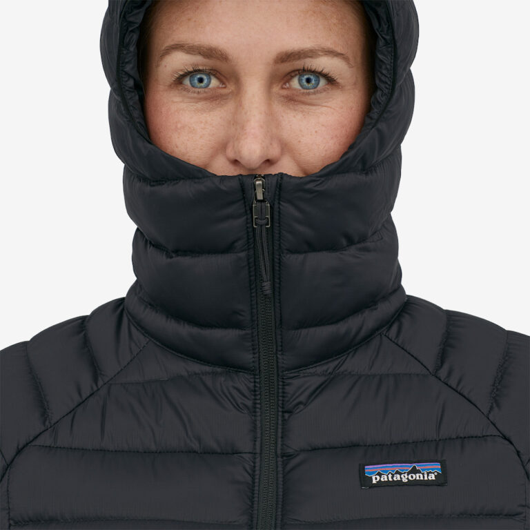 A woman with bright blue eyes is wearing a black hooded jacket with the hood up, with the brand logo Patagonia on the jacket.