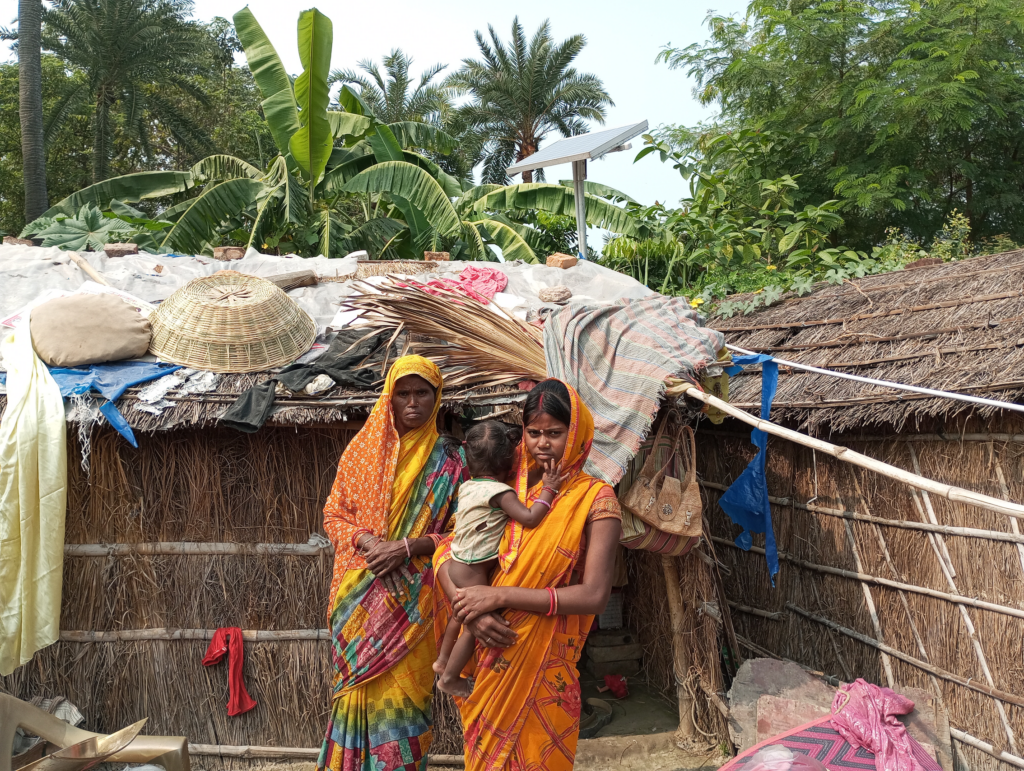 Two women and a baby stand outside their home.